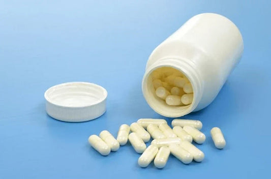  Probiotic capsules spilling from open white bottle on a blue background