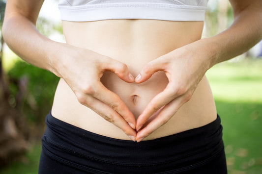 Close-up of a woman's hands forming a heart shape over her stomach, symbolizing gut health.