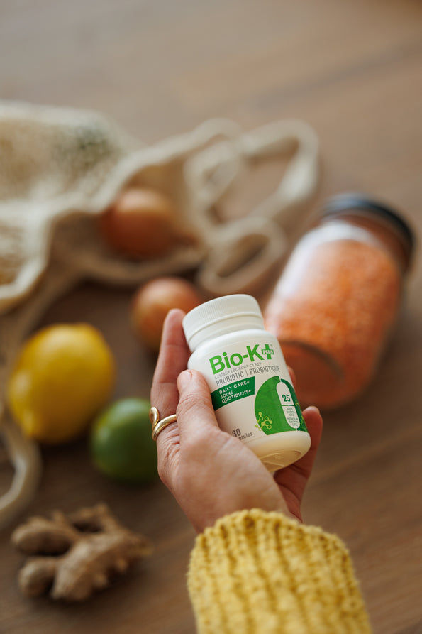 Hand with Bio-K+ capsules, we can see fruits and vegetables in the backgroud