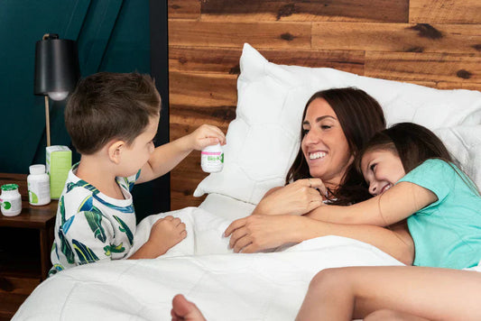 A mother in bed with her daughter hugging her and her son handing her a bottle of Bio-K+ drinkable.