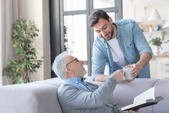 Older man relaxing on sofa receiving a cup of tea from a smiling younger man at home
