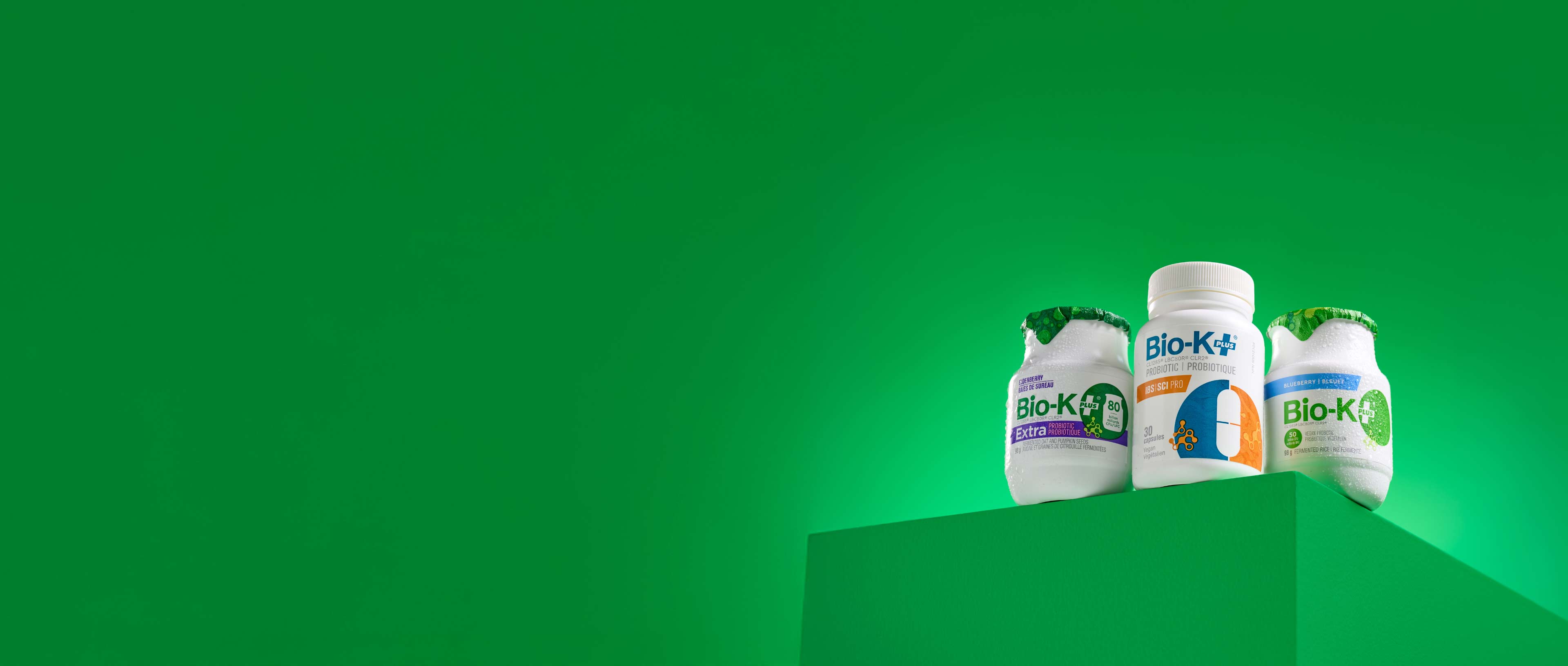 Three Bio-K supplement bottles on a green background