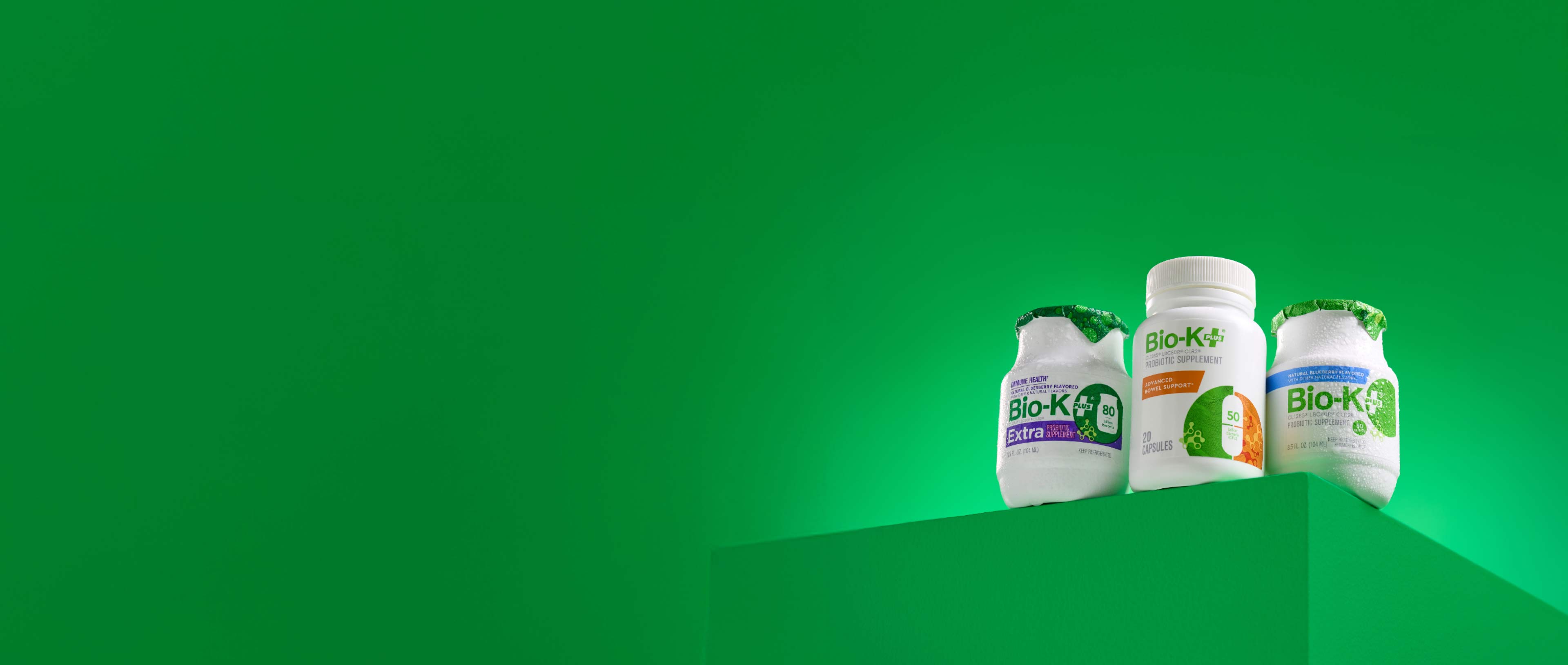 Three Bio-K supplement bottles on a green background